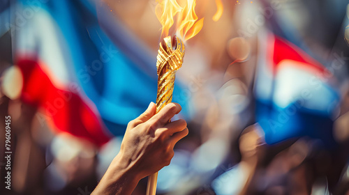 Hand holding the Olympic torch with an abstract French flag background
