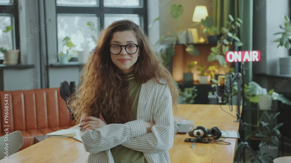 Young beautiful girl with long hair holding arms crossed and looking at camera with smile in podcast recording studio. Video portrait Young beautiful girl with long hair holding arms crossed and looking at camera with smile in podcast recording studio. Video portrait