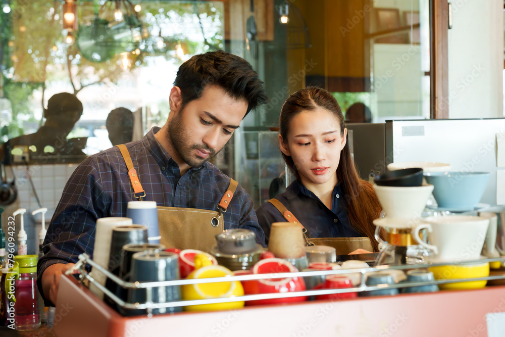 Beautiful Asian woman with Hispanic man concentrating on making orders that the customer has ordered intentionally. It's at the counter with a coffee machine at their business cafe.