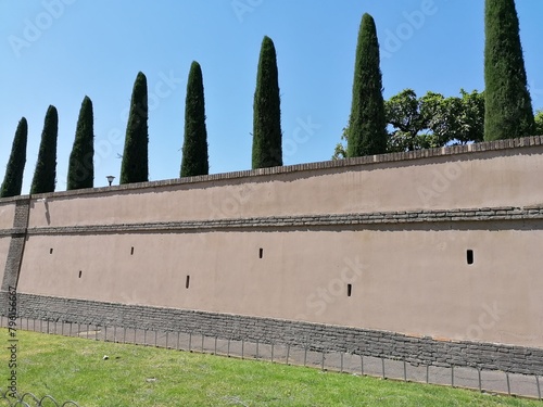 View of a portion of a perimeter wall of a large villa, with cypress trees, in the city center.