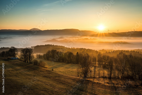 The sun illuminates a valley with thick inversion fog, wind farms and the Královecký špičák mountain in the background on a cold morning in early autumn near Trutnov © Simona_Mach