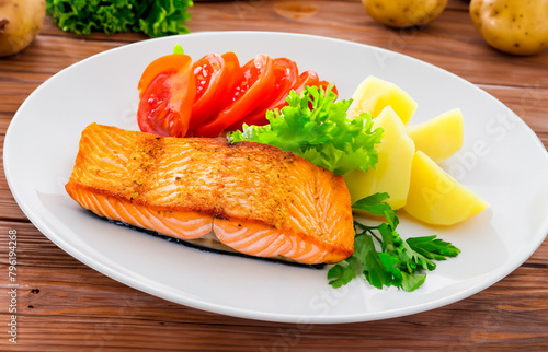 Fried salmon steak with potatoes and vegetables on a wooden table