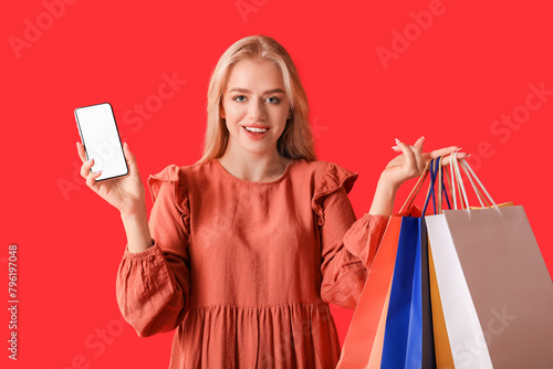 Young woman with mobile phone and shopping bags on red background