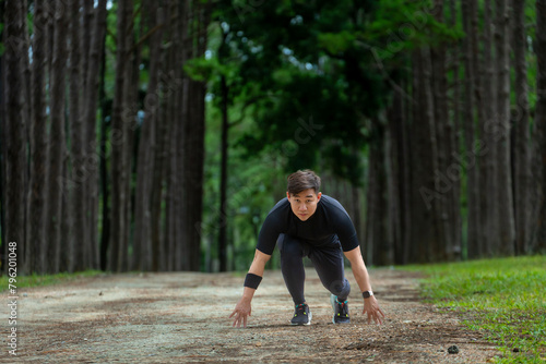 Asian trail runner is running outdoor in pine forest dirt road for exercise and workout activities training while concentrate on the start position to race for healthy lifestyle and fitness concept