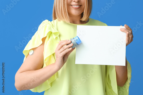 Woman with glucose sensor for measuring blood sugar level and blank paper on blue background. Diabetes concept