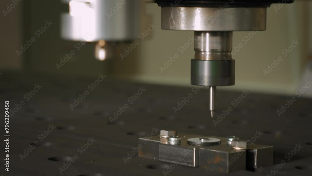 Drill Bit is moving Horizontally and Vertically. Cutting through the Metal Working Piece Fixed on the Table. Drilling Machine. Machining Process. Manufacturing Facility. Production of Radios. Close up Drill Bit is moving Horizontally and Vertically. Cutting through the Metal Working Piece Fixed on the Table. Drilling Machine. Machining Process. Manufacturing Facility. Production of Radios. Close up