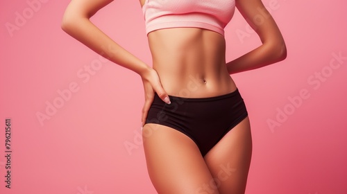 Close-up of fit woman's torso with her hands on hips against a pink background. © Natalia