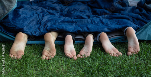 three pairs of cute bare feet of children sticking out of sleeping bag. Children, siblings or friends lie side by side in tent . Healthy lifestyle, little tourist, family vacation, summer fun