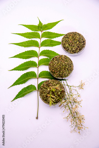 Close up top view of Indian ayurvedic herb Neem /Azadirachta Indica green leaves on white background with dry powder in glass dish with selective focus.Medicinal Neem leaves with neem paste in spoon  photo