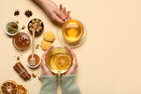 Female hands holding cups of tea, jam, honey and cookies on beige background