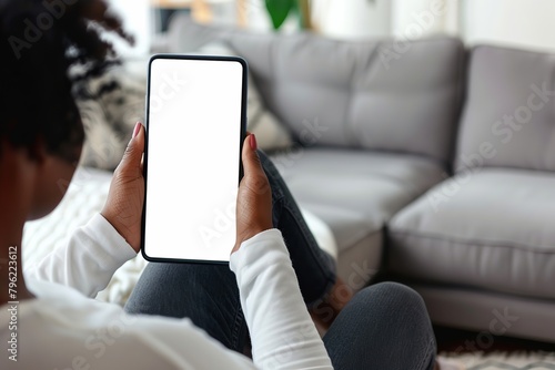 Woman using a Smart Phone with White Screen. Back view of Girl wear Jeans sitting in Living room using Mobile Phone Chroma Key Screen. African American Female is watching, looking at WhiteScreen Phone