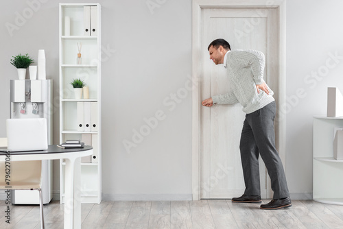 Young businessman suffering from back pain at door in office