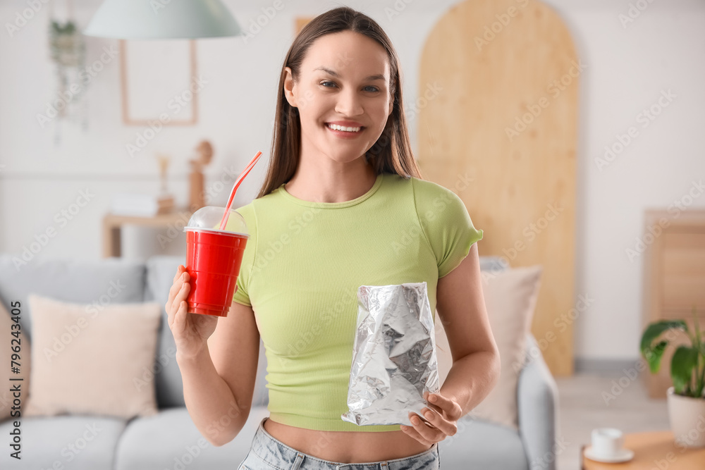 Young woman with potato chips and soda at home