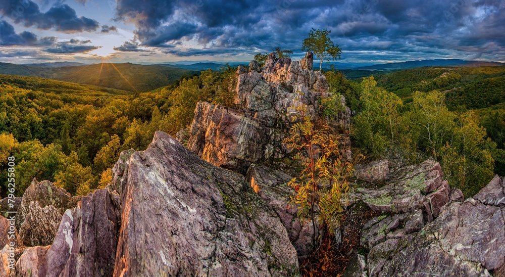 Obraz premium Sunset in forest with rocky mountain hill. Dramatic, colorful sunset in the autumn landscape. Bizarre, colorful rocks, illuminated hills and trees, beautiful sky. Tribec, Oselny vrch, Slovakia.