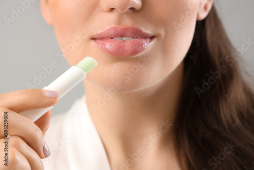 Young woman with lip balm on grey background  closeup