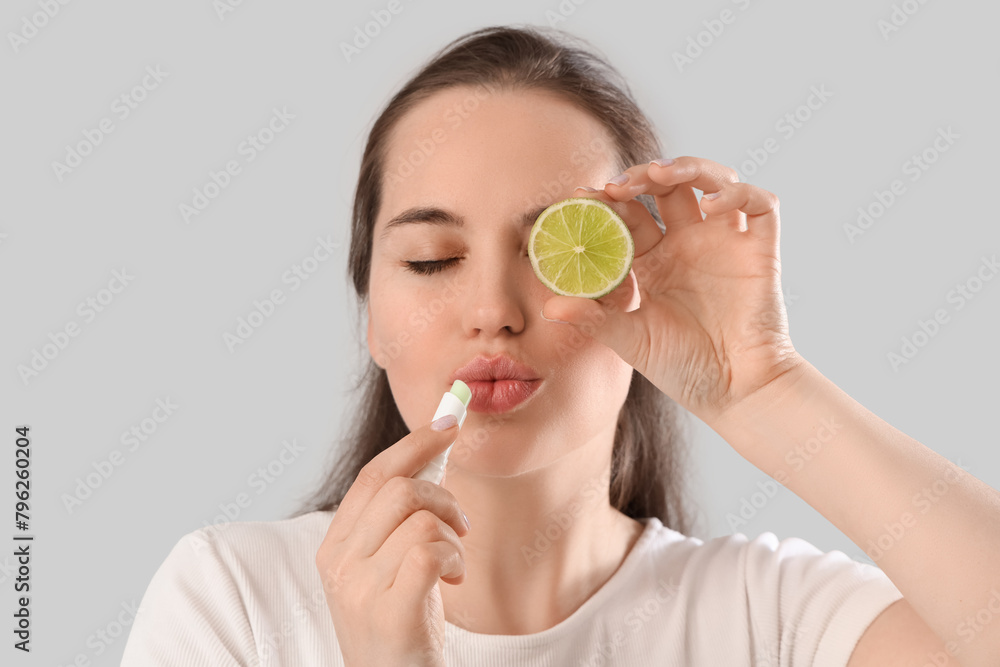 Young woman with lime applying lip balm on light background, closeup Young woman with lime applying lip balm on light background, closeup