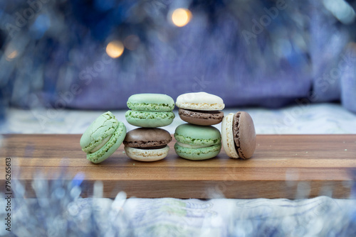 Close up delicious macaroon cookies in fresh mint green vanilla beige chocolate brown colors. Blue bokeh shining blurred foreground decor, wooden table. Contrast bright combination, bakery culinary.