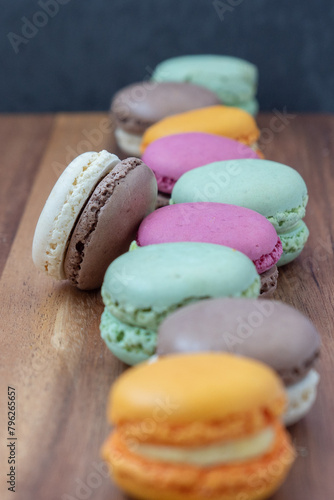 Close up delicious macaroon cookies in fresh mint green vanilla beige chocolate brown orange and pink colors. Shallow depth, vertical frame, wooden table. Contrast bright combination, bakery culinary.