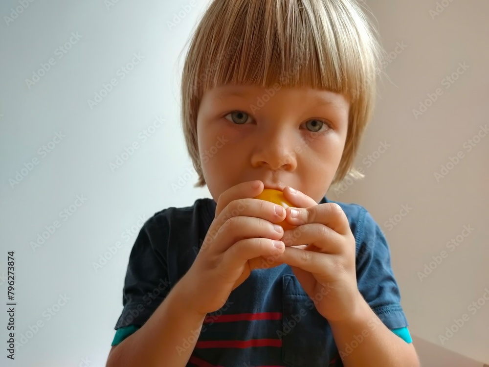 Little child holding tomatoes in his hand and eating and having fun with them on grey background. The child eats and holds vegetables and tomatoes Little child holding tomatoes in his hand and eating and having fun with them on grey background. The child eats and holds vegetables and tomatoes