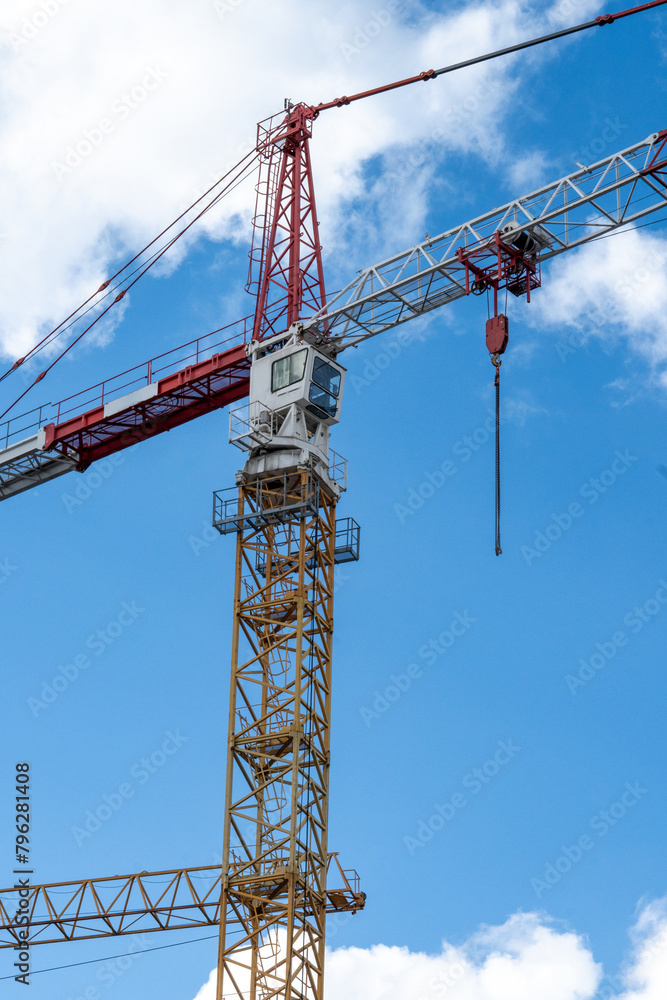 Tower crane with operator's cabin against a blue sky with white clouds Tower crane with operator's cabin against a blue sky with white clouds