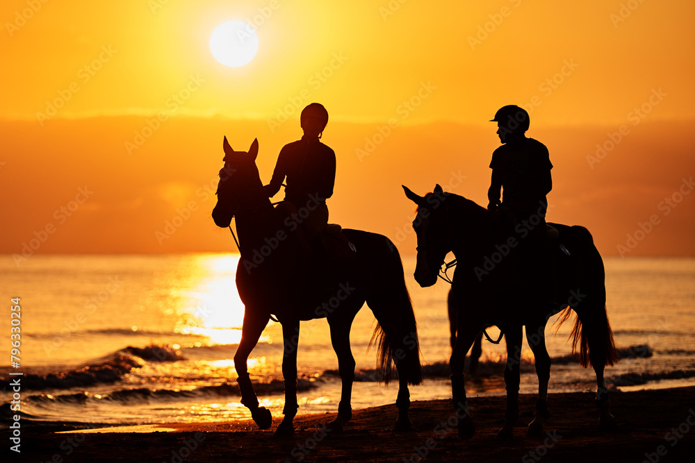 Riders in silhouette at the beach excercising horses