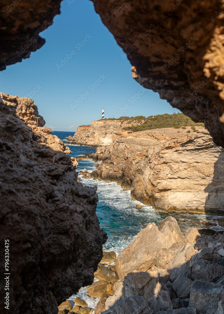 Punta Moscarter lighthouse seen through a rock hole in a cave near Portinatx, Sant Joan de Labritja, Ibiza, Balearic Islands, Spain