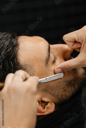 A man sitting in a barber shop getting his beard shaved by the barber