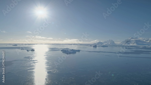 Aerial Drone Flight Over Antarctica Ocean. Sun Track and Bright Sun Disk. Breathtaking Polar White Blue Landscape. Ice Cold Water, Snow Covered Mountains of Antarctic Continent.