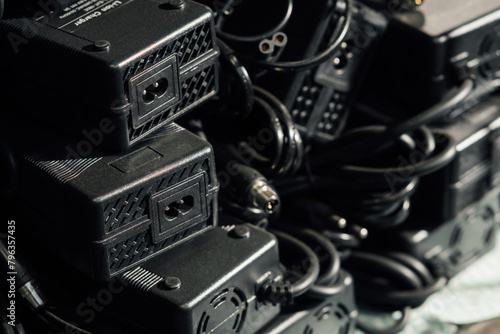 Close up view of the shelf with power adapters. AC to DC converter for e-bikes. Black plastic rectangular boxes with cables at the shelf at the electronics warehouse