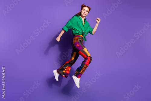 Full size photo of girlish cheerful woman dressed vintage pants running look at promotion empty space isolated on purple color background