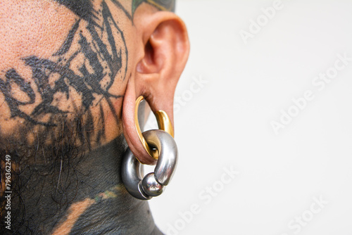 Closeup shot of a gold flesh tunnel, also known as a earplug, earspool. Large gauge plug on the earlobe of a man with face tattoos. photo