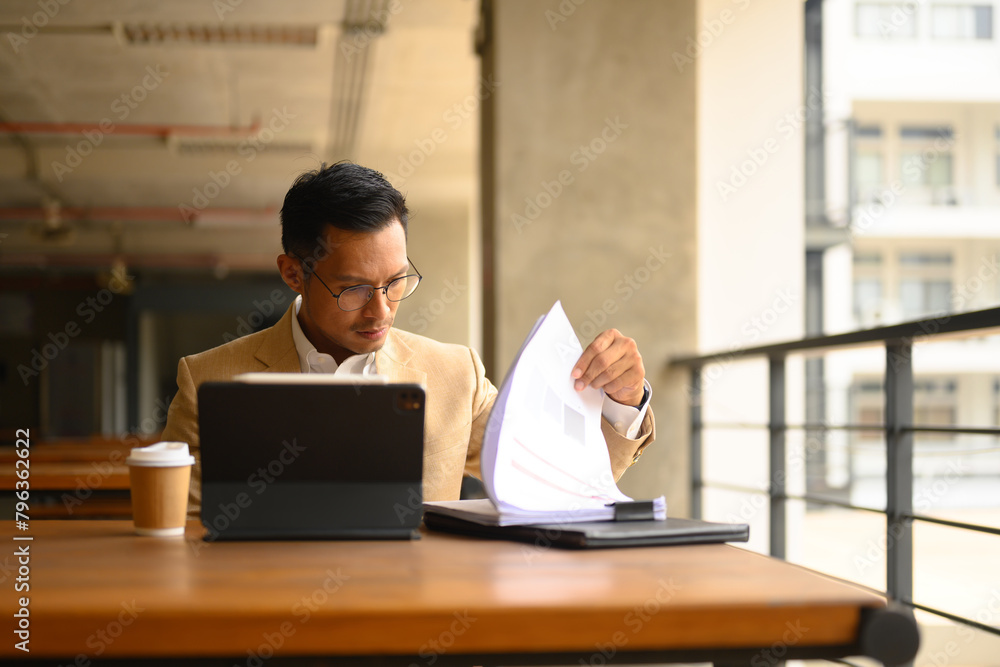 Serious busy businessman reading financial documents and working with digital tablet Serious busy businessman reading financial documents and working with digital tablet