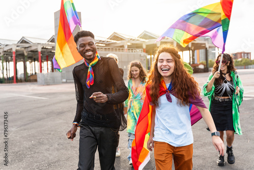 A happy crowd of people is walking down the street holding rainbow flags, enjoying the event and spreading joy with smiles and fun