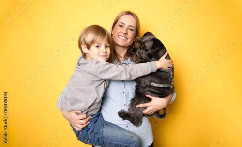 Happy mother with her son and schnauzer dog standing isolated on yellow background.