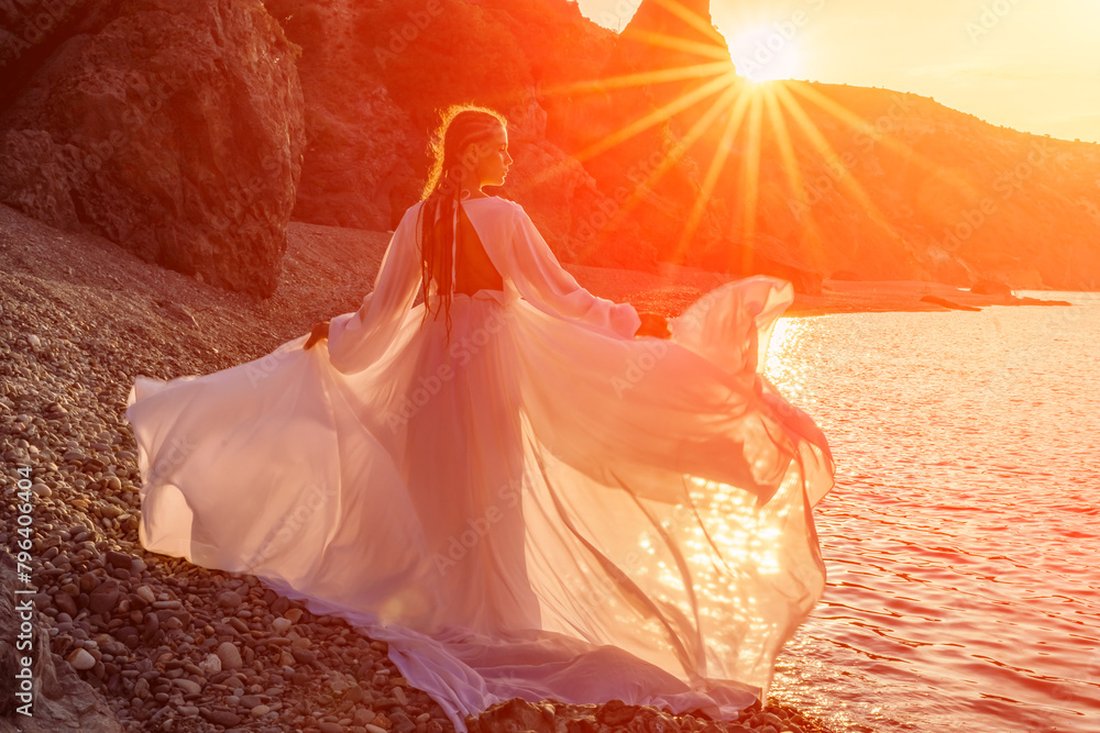 Mysterious woman silhouette long hair walks on the beach ocean water, sea nymph wind listens to the wave. Throws up a long white dress, a divine sunset. Artistic photo from the back without a face Mysterious woman silhouette long hair walks on the beach ocean water, sea nymph wind listens to the wave. Throws up a long white dress, a divine sunset. Artistic photo from the back without a face