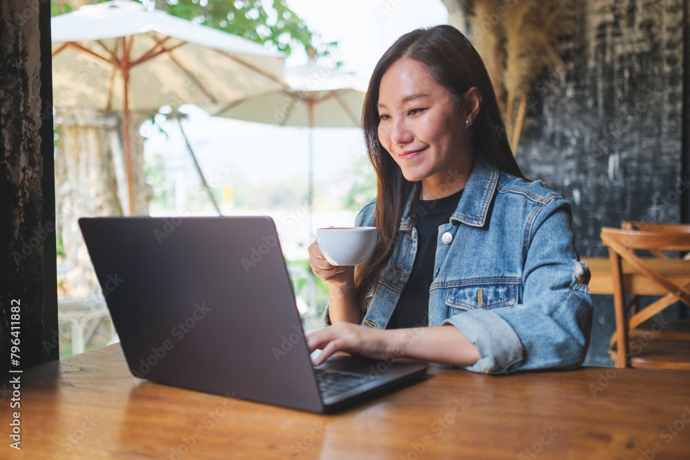 Portrait image of a young woman drinking coffee while working on laptop computer in cafe Portrait image of a young woman drinking coffee while working on laptop computer in cafe