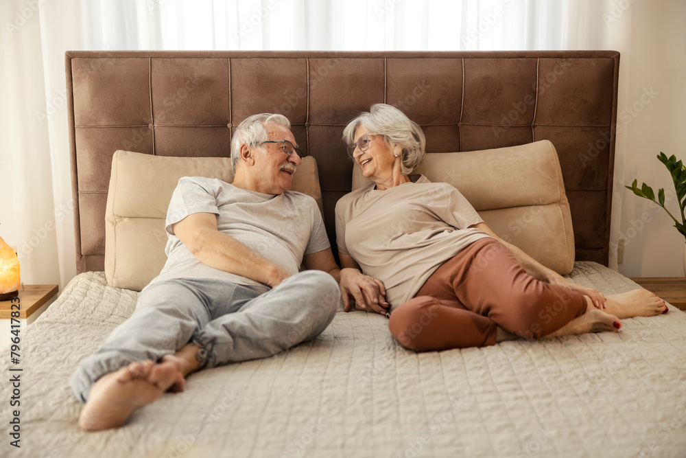 Senior couple laying down on a bed in a bedroom and relaxing.