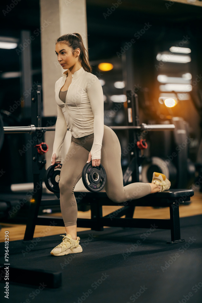 A strong fit athlete is working out with weight plates split squats in a gym. A strong fit athlete is working out with weight plates split squats in a gym.