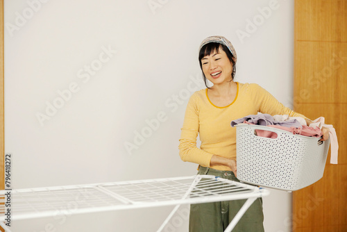A tidy japanese housewife holding basket with clothes and doing laundry at home.