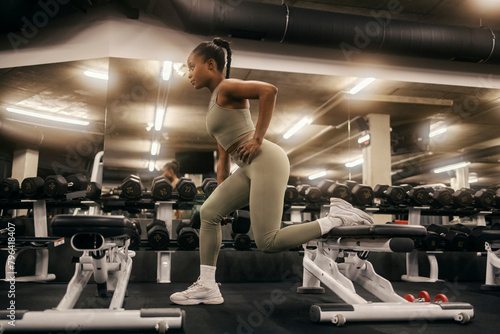 An active powerful african american sportswoman doing bulgarian lunges at gym.