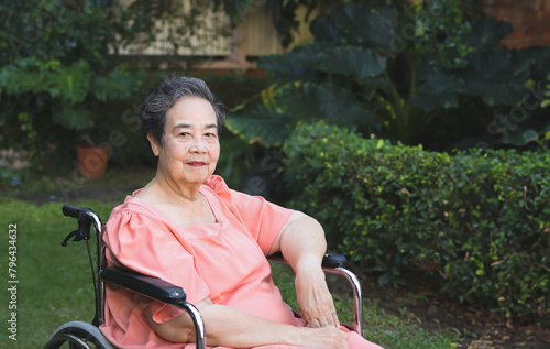 Happy Asian senior woman sitting on wheelchair  in the garden, smiling and looking at camera.