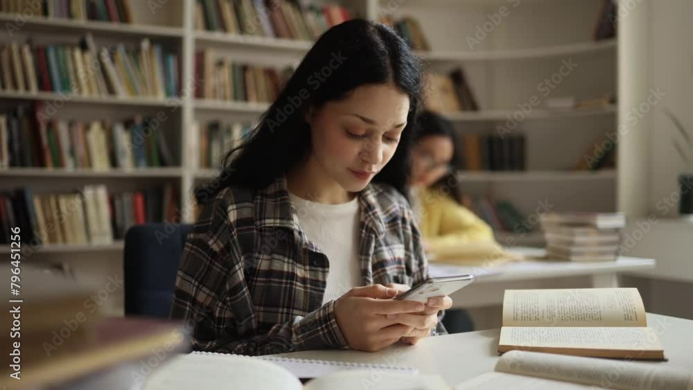 Smiling young woman hold smartphone scrolling social media online while take a break at university library Pretty student relax enjoying great day after lessons indoors Smiling young woman hold smartphone scrolling social media online while take a break at university library Pretty student relax enjoying great day after lessons indoors