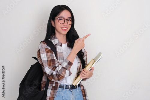 Female college student holding books smiling and pointing beside her