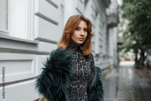 Beautiful red-haired woman model in fashionable clothes walks in the city