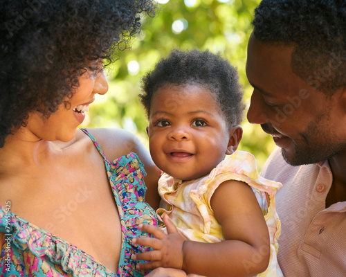 Close Up Of Loving Parents Cuddling Baby Daughter Outdoors In Garden Or Countryside Together photo