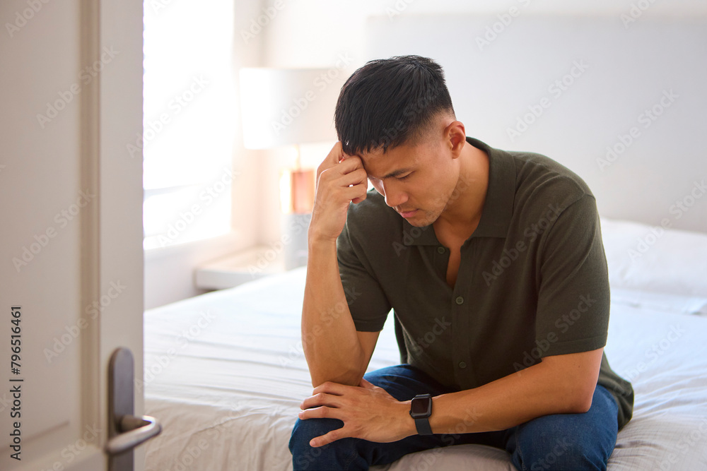 Unhappy Or Depressed Man Sitting On Bed At Home With Head In Hands