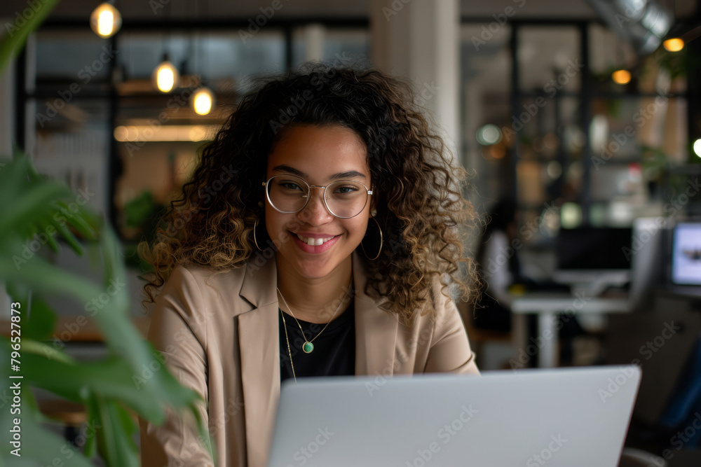 Happy Latino woman using a laptop in a brightly lit office, showing success and positivity. Happy Latino woman using a laptop in a brightly lit office, showing success and positivity.