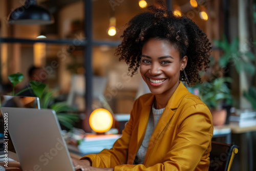 Smiling Black woman typing on a laptop in a well-lit office, exuding success and positivity.