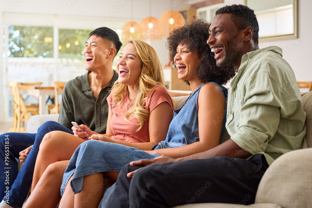 Group Of Multi-Racial Friends Sitting On Sofa Laughing Watching Movie Or Show On TV Together