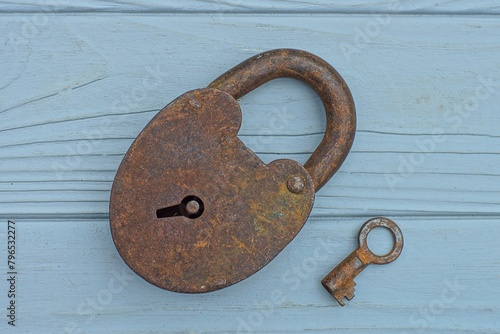one old rusty reliable iron hinged closed large with a key retro dirty lock lies on a gray wooden table